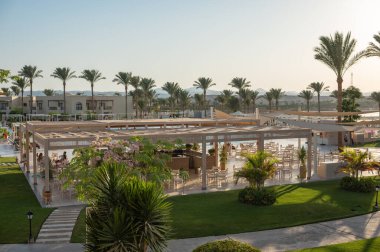 MMarsa Alam, Mısır 19.07.2025 - Mısır 'ın Marsa Alam kentindeki tropik bir tatil beldesinde altın gün batımı, palmiye ağaçları, yeşil çimenler ve deniz. Düzenleyici kullanımı