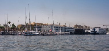 Luxor, Mısır - 27.07.2025. Geleneksel Felucca yelkenli tekneleri ve diğer tur tekneleri Nil Nehri 'ndeki kalabalık bir rıhtıma yanaştı, turistler için hazırlar.