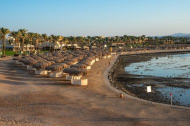 Marsa Alam, Mısır 19.07.2025 - Sığ ve kayalık bir körfezin panoramik görüntüsü, arka planda bir tatil köyü, palmiye ağaçları ve dağların alçak bir gelgiti ortaya çıkarıyor. Düzenleyici kullanımı