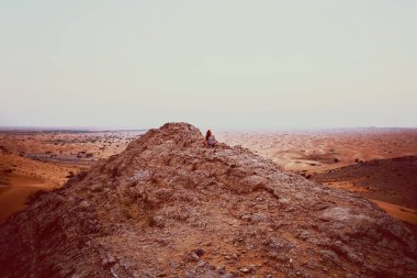 Büyük taş kayadaki küçük kadın figürü Dubai Al Awir çölünde, manzaralı günbatımı manzarası