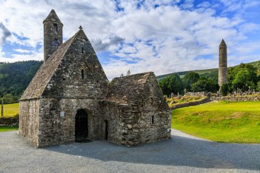 Glendalough, St. Kevin tarafından 6. yüzyılda kurulan erken ortaçağ manastırı yerleşimi. Aziz Kevin Kilisesi 'nin arka planında mezarları ve yuvarlak kulesi var..