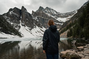 Kadın gölün kenarında durur dramatik karlı dağ zeminine bakar