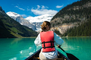 Turkuaz buzul gölünde kano, karla kaplı dağlar ve çam ormanlarıyla çevrili.