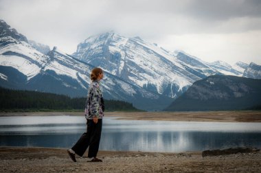 Lone wanderer by serene lake, majestic snow-capped mountains. Outdoor beauty and tranquility.