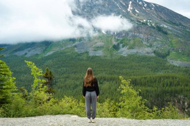 A woman stands on a scenic overlook, gazing at a majestic mountain