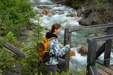 A hiker crosses a rustic wooden bridge over a rushing stream