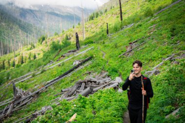 Hiker pauses to capture the view while trekking a lush mountain trail.