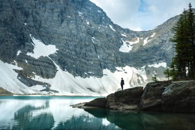 Person overlooking a serene alpine lake with snow-capped mountains in the background