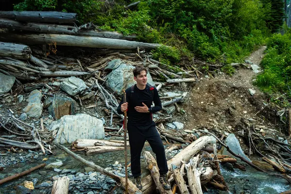 Adventurous hiker with a walking stick crosses a stream amidst a debris-filled landscape.