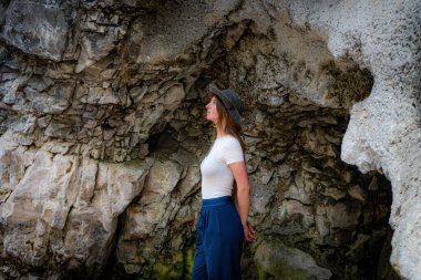 Contemplative woman in cave, looking up with a hat, wearing casual clothes.