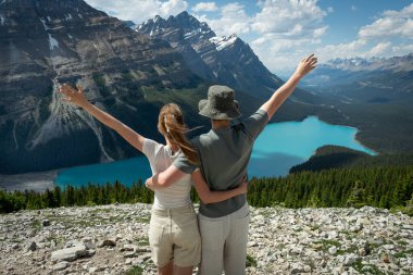 Couple embracing with arms raised overlooking a turquoise lake and mountains.