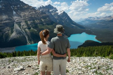 Couple admiring mountain lake scenery from a rocky overlook, arm in arm.
