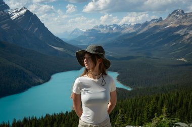 Woman in hat enjoying mountain view with turquoise lake in background.