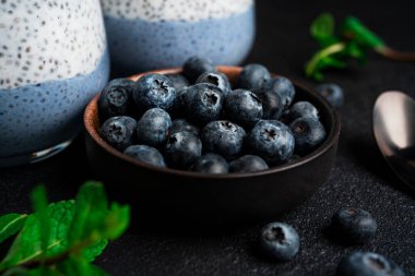 Arka planda yaban mersinli Chia pudingi. Siyah arka planda Chia pudingi, nane ve yaban mersini. Yüksek kalite fotoğraf