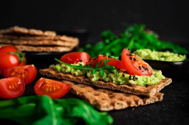 Avokado sandviçi, avokado kremalı ve abur cubur için çavdar ekmekli. Fiber, fitness ve diyet yiyecekler. Çavdar ekmeği, guacamole, roka ve koyu arkaplanda vişneli domates. Yüksek kalite fotoğraf