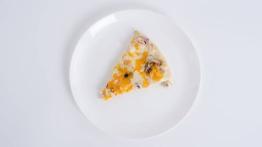 Renkli peynirli, jambonlu ve mantarlı bir dilim pizza sade beyaz bir tabakta duruyor. Taze malzemeler, cezbedici yemeklere vurgu yapıyor..