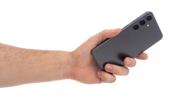 Bir insan, üç arka kamerası olan modern bir akıllı telefonu tutmak için elini uzatır. Gösterişli cihaz düz bir arkaplan üzerinde sergileniyor, tasarımıyla işlevselliğini vurguluyor.