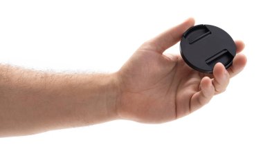 Bir el, parlak siyah yüzeyini gösteren dairesel bir lens kapağını kavrıyor. Şapkaya odaklanmış, tasarımı ve amacı vurgulanıyor. Bu an basitliği ve işlevselliği yakalar.