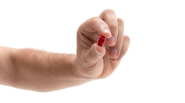 Bir el, kırmızı kapsülü iyi aydınlatılmış koşullarda kavrıyor ve ilaca odaklandığını gösteriyor. Arkaplan nötr, kapsülün enerjisini arttırıyor..