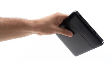 Bir el, modern tasarımını sergileyen şık, taşınabilir bir aleti kavrıyor. Kullanıcı bağlı görünüyor, bu da teknolojiyle bir etkileşim anını gösteriyor. Yumuşak ışıklandırma aygıtların özelliklerini vurgular.