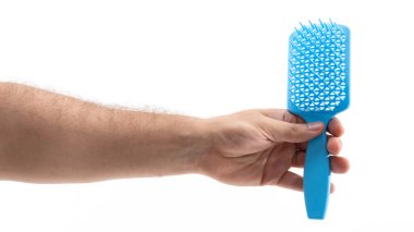 Bir insan eli canlı mavi bir saç fırçasını kavrayıp ince dişlerini ve ergonomik tasarımını sergiliyor. Arkaplan tamamen beyaz, fırçaların rengini ve detaylarını vurguluyor.