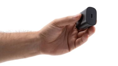 Bir el parlak siyah bir şarj aletini tutuyor. Şarj aleti tek bir porta sahiptir ve elektronik cihazların kullanışlı şarjı için tasarlanmıştır. Arkaplan sade ve sade..