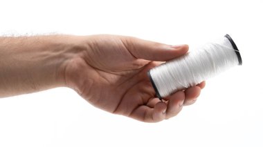 Düz bir arkaplanda beyaz bir dikiş ipliğini tutan bir el. İplik düzgün bir şekilde yaralanmış, dokusunu ve parıltısını sergiliyor, dikiş işçiliğini vurguluyor..