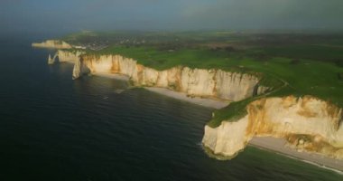 Deniz kıyısındaki tebeşir uçurumlarının insansız hava aracı görüntüsü. İnsanlar okyanustaki yeşil kayalar boyunca yürür. Fransa 'da bir dönüm noktası. Etretat, Normandiya İHA 'sından hava görüntüsü.