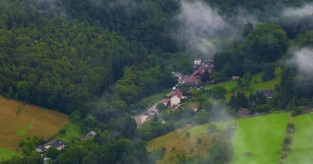 ドイツ ドイツの丘のヨーロッパの雲と緑の新鮮な森の上を飛行するドローン ドイツの霧の森の周りの空中ビュー 春の曇った日 森林地帯に位置する静かなドイツの村 — ストック動画