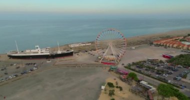 Yazın Les Barcarele plajının havadan görünüşü. Turizm sezonu, plajda bir dönme dolap ve turistlerin ilgi odağı olan büyük bir gemi var..