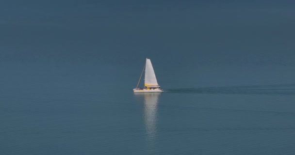 天気の良い海の青い表面に沿って航海する白い帆を持つヨットのドローンからの眺め — ストック動画