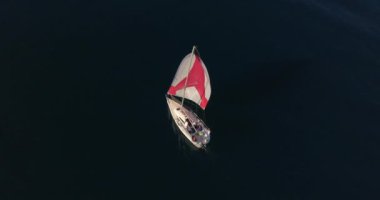 Yacht sailing on open sea with red sails aerial view. Nature seascape with sail boat cruising at ocean bay. Cinematic summer vacation scenery.