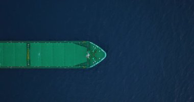 Mavi okyanus üzerinde hızla seyahat eden büyük bir kargo gemisinin baş omuzluğunun yukarıdan görünüşü. Denizde ultra büyük gemi görüntüsü oluşturuluyor. Kargo gemisi limandan ayrılıyor..