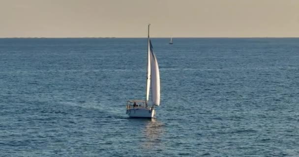 青い暖かい水の白いモダンなヨット 船のドローンから海の深さを耕す帆を眺める 太陽が沈む光の中で海を旅する 贅沢なライフスタイル — ストック動画
