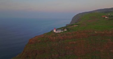 Güneş batarken, Madeira, Portekiz 'de kayalık kayalıklardaki havadan kırmızı ve beyaz deniz feneri binasına..