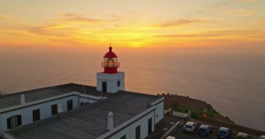 Güneş batarken, Madeira, Portekiz 'de kayalık kayalıklardaki havadan kırmızı ve beyaz deniz feneri binasına..