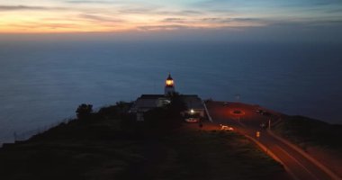 Alacakaranlıkta çalışan deniz fenerine açılan hava manzaralı bir kaya parçası. Deniz feneri Ponta do Pargo, Madeira Portekiz.
