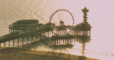 Hava aracı Kuzey Denizi kıyısı Scheveningen İskelesi 'nde gün batımını ve ünlü dönme dolap SkyView de Pier, Den Haag, Hollanda. Hollanda 'daki merkezin ufuk çizgisi.