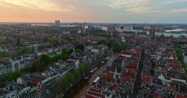 Avrupa turizm şehri Amsterdam 'ın havadan görünüşü. Gün batımında şehir merkezinde bir dron uçuyor. Hollanda 'nın en büyük ve en ünlü şehrinin çekimleri yapılıyor. Dar kanallar şehri böler.