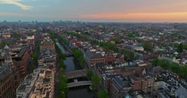 Avrupa turizm şehri Amsterdam 'ın havadan görünüşü. Gün batımında şehir merkezinde bir dron uçuyor. Hollanda 'nın en büyük ve en ünlü şehrinin çekimleri yapılıyor. Dar kanallar şehri böler.