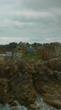 Brittany 'de okyanusta kayalıklarda bir ev. Atlantik okyanusunun kayalık kıyılarının havadan görünüşü, okyanus alçak gelgit, sudaki kayalar. Plougrescant uçurumu.