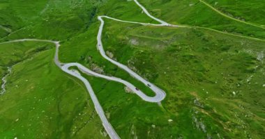 İsviçre dağları boyunca seyahat eden turistlerin hava manzarası keskin virajlar boyunca devam ediyor. Hava aracı manzaralı, çayırların arasından dönen dağ yolu. İsviçre Alplerinde yılan yolu.