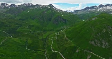 İsviçre dağları boyunca seyahat eden turistlerin hava manzarası keskin virajlar boyunca devam ediyor. Hava aracı manzaralı, çayırların arasından dönen dağ yolu. İsviçre Alplerinde yılan yolu.