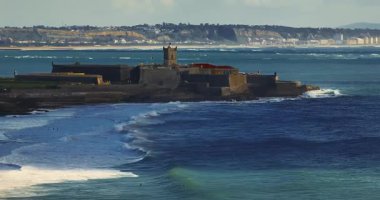 Arka planda ünlü bir köprü olan Portekiz 'deki bir kalenin insansız hava aracı görüntüsü. Portekiz, Carcavelos sahilinden deniz feneri kulesi olan Aziz Julian Kalesi. Carcavelos 'taki Atlantik okyanus dalgaları plajı.