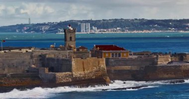 Arka planda ünlü bir köprü olan Portekiz 'deki bir kalenin insansız hava aracı görüntüsü. Portekiz, Carcavelos sahilinden deniz feneri kulesi olan Aziz Julian Kalesi. Carcavelos 'taki Atlantik okyanus dalgaları plajı.
