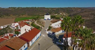 Yel değirmeni ve pitoresk çatıları olan küçük köyün havadan görünüşü, Aldatmaca, Portekiz.