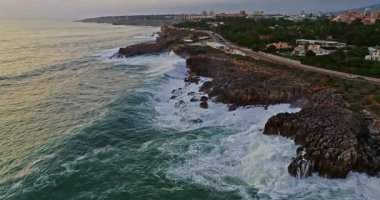 Cascais, Portekiz 'de deniz kıyısında kayalık sahile vuran hava manzaralı dalgaların altında.
