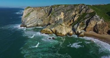 Büyük kayalıkların üzerine köpüklü dalgaların düştüğü Ursa sahili Atlantik sahil sörfü. Portekiz.