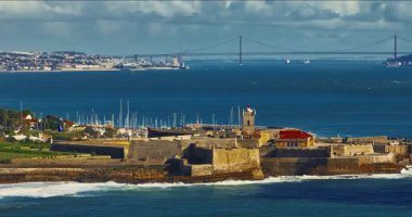 Arka planda ünlü bir köprü olan Portekiz 'deki bir kalenin insansız hava aracı görüntüsü. Portekiz, Carcavelos sahilinden deniz feneri kulesi olan Aziz Julian Kalesi. Carcavelos 'taki Atlantik okyanus dalgaları plajı.