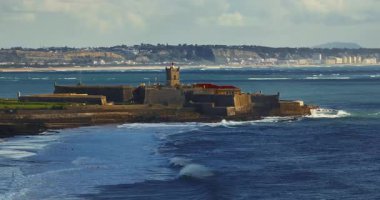 Arka planda ünlü bir köprü olan Portekiz 'deki bir kalenin insansız hava aracı görüntüsü. Portekiz, Carcavelos sahilinden deniz feneri kulesi olan Aziz Julian Kalesi. Carcavelos 'taki Atlantik okyanus dalgaları plajı.